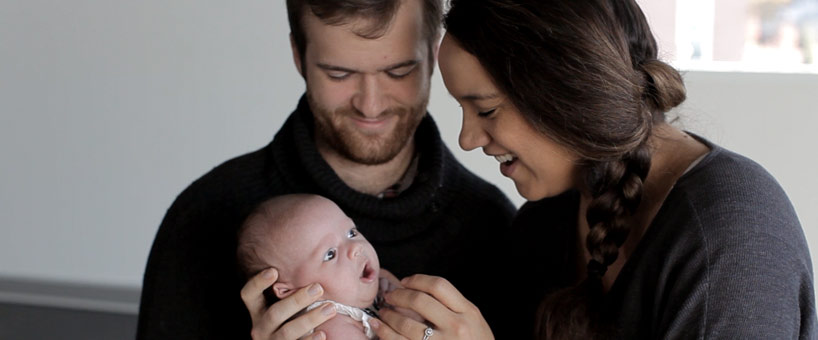 White man and islander woman looking at smiling at baby